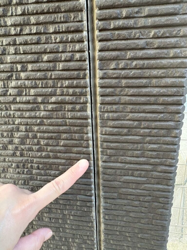 外壁の隙間を指で示している様子｜コーキングの劣化によるひび割れ（羽村市）